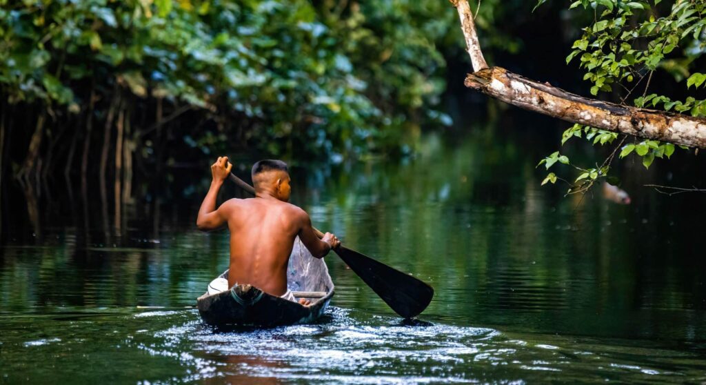 Native,Tribal,Man,Swimming,In,Amazonia,Rainforest,In,Handmade,Boat