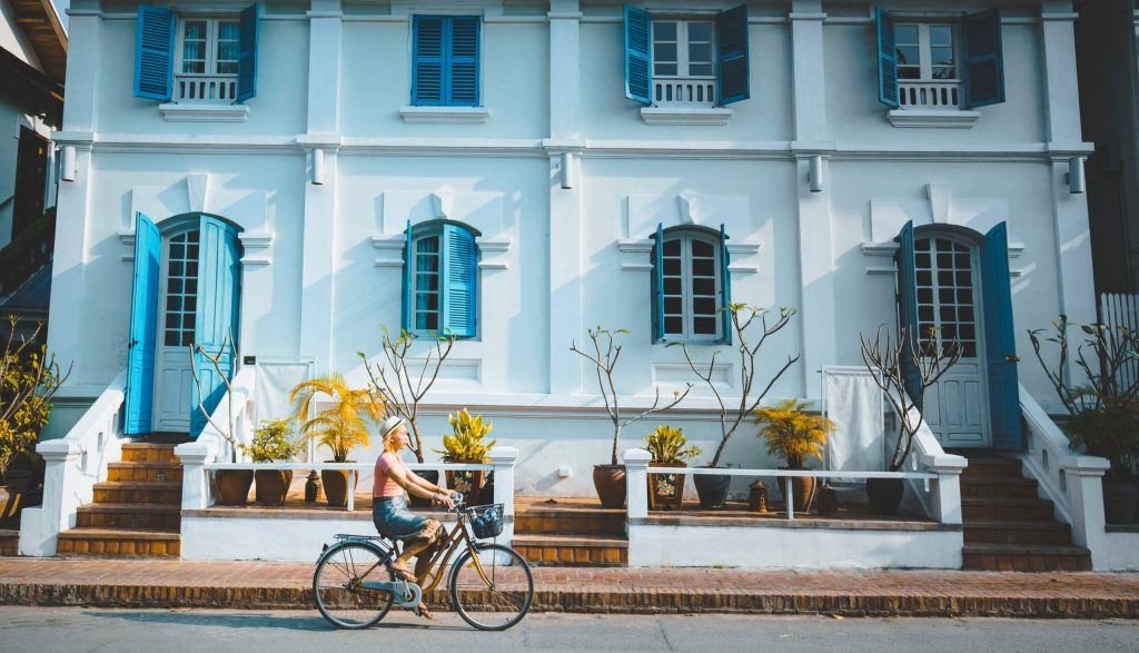 Young,Woman,Standing,With,Bicycle,In,Front,Of,Colonail,Style