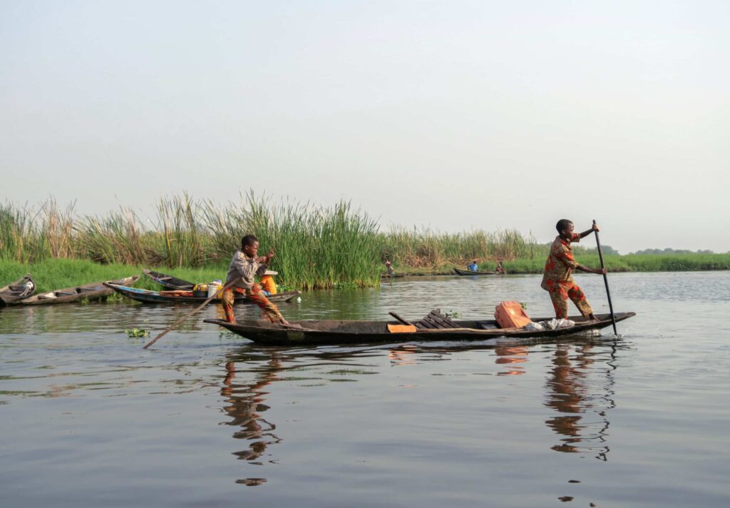 Deux jeunes hommes naviguant sur le lac Ahémé au coucher du soleil.