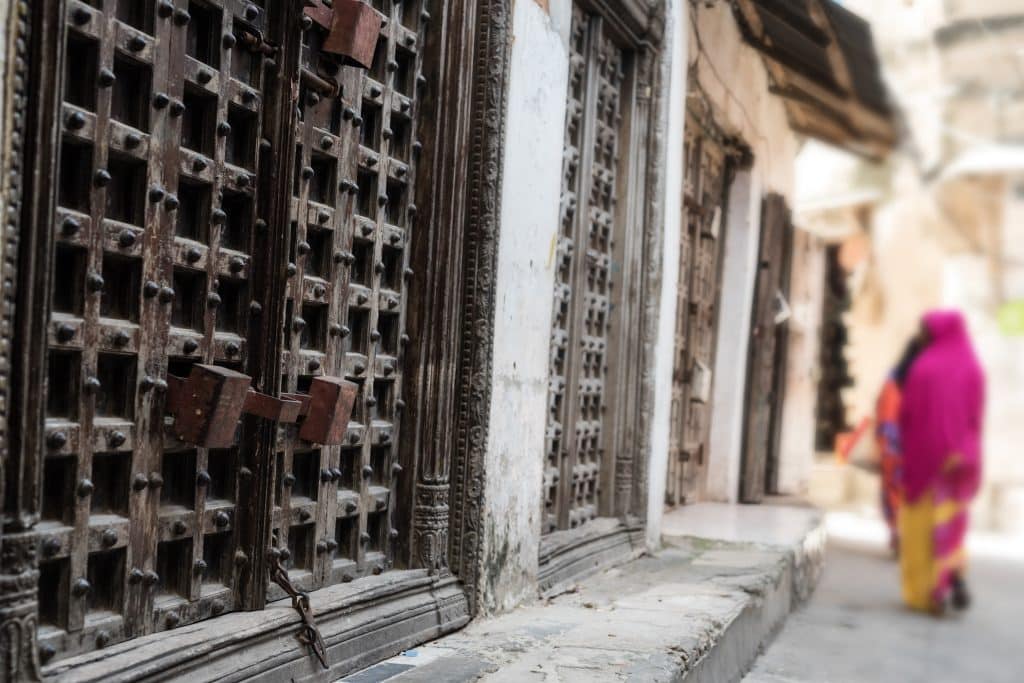 Typical,Zanzibar,Town,Street,With,Old,Iron,Doors,And,Wooman